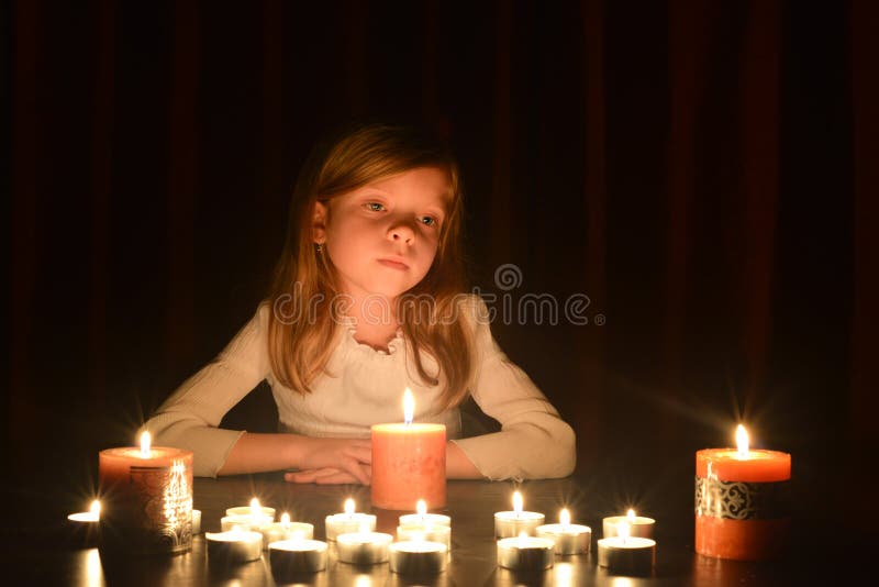 La petite fille blonde mignonne regarde sur la lumière de la bougie Un bon nombre de bougies sont autour de elle, au-dessus du fo photos libres de droits La petite fille blonde mignonne regarde sur la lumière de la bougie Un bon nombre de bougies sont autour de elle, au-dessus du fo photos libres de droits