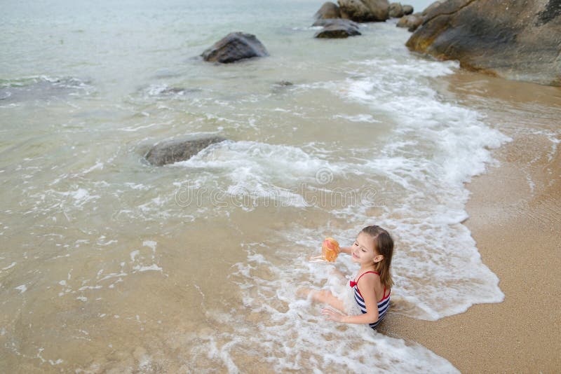 La petite fille caucasienne s'asseyant avec la poupée sur le sable en mer ondule dans le matin images stock La petite fille caucasienne s'asseyant avec la poupée sur le sable en mer ondule dans le matin images stock