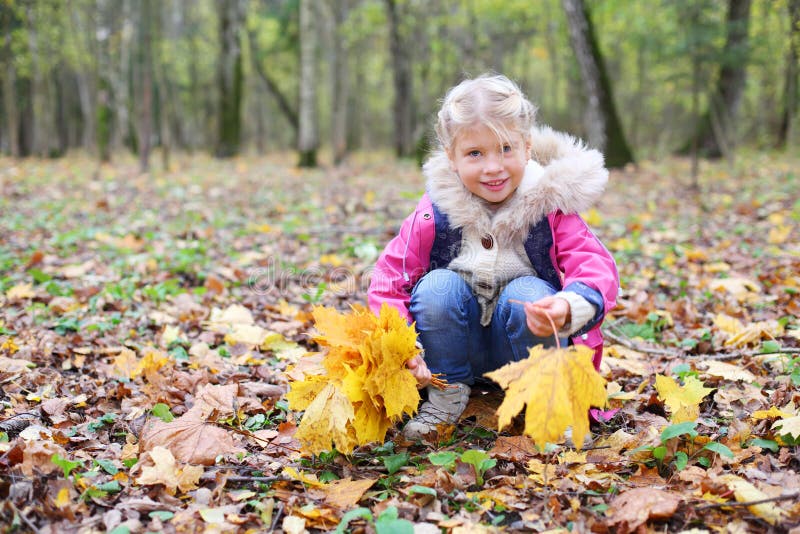 La petite fille de sourire s'accroupit et tient des tracts d'érable image stock La petite fille de sourire s'accroupit et tient des tracts d'érable image stock