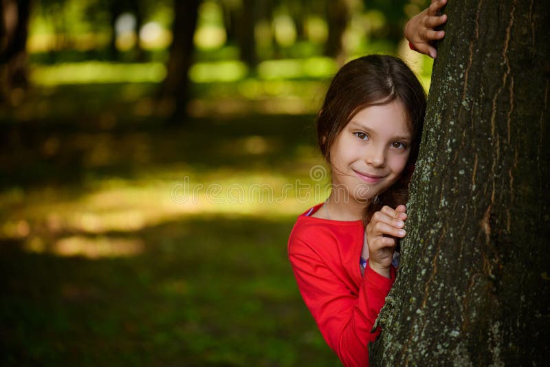 La petite fille de sourire se cache derrière l'arbre image libre de droits La petite fille de sourire se cache derrière l'arbre image libre de droits