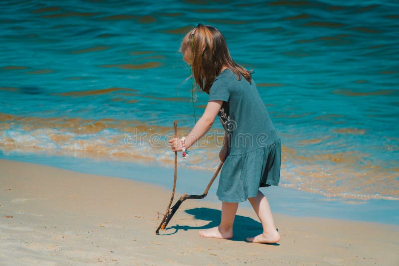 La petite fille dessine sur le sable à la plage photographie stock libre de droits La petite fille dessine sur le sable à la plage photographie stock libre de droits