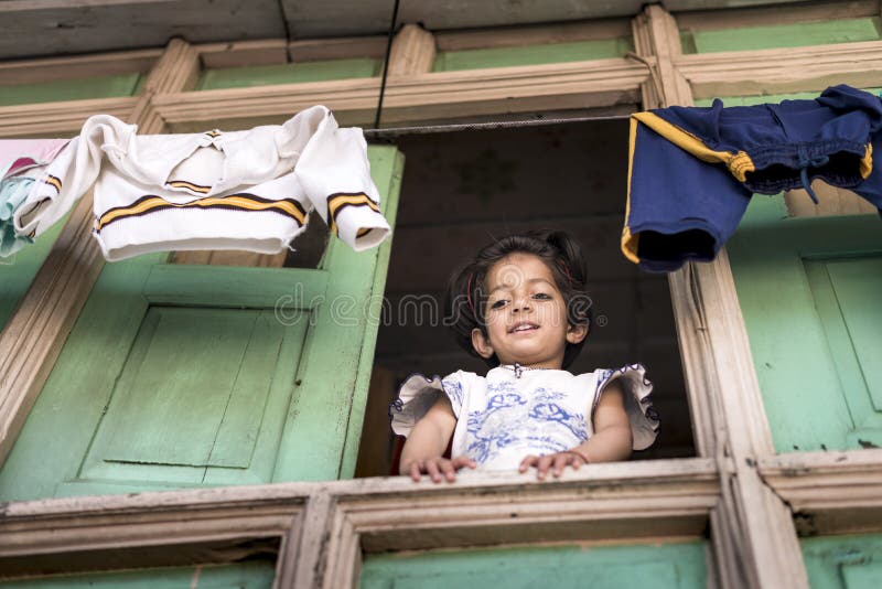 La petite fille douce regardent fixement vers le bas de sa fenêtre en bois de maison avec les vêtements accrochants en haut images stock La petite fille douce regardent fixement vers le bas de sa fenêtre en bois de maison avec les vêtements accrochants en haut images stock