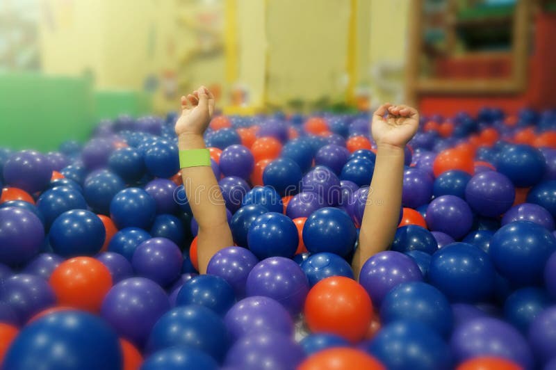 The little girl is under a plastic ball in Ball pit. She lifted her arms and made fun sounds. The little girl is under a plastic ball in Ball pit. She lifted her arms and made fun sounds.