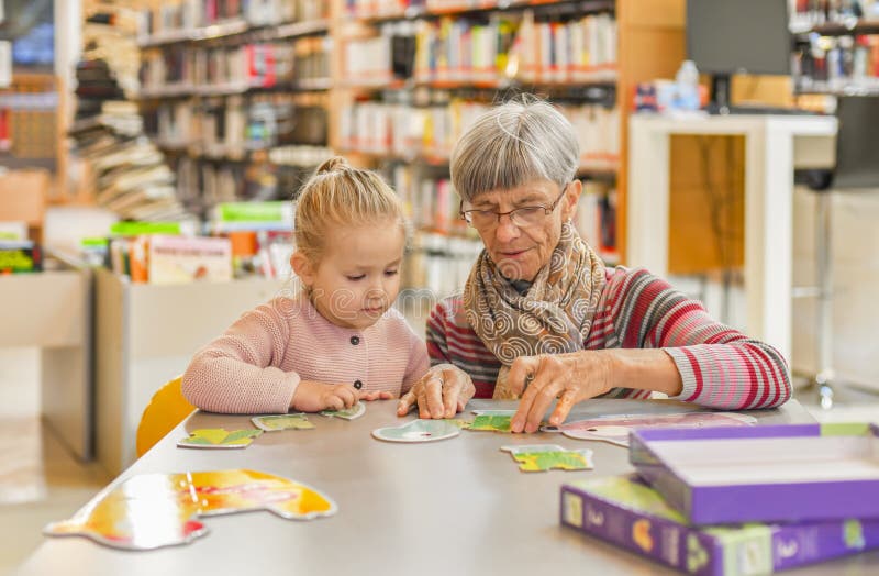 La petite-fille et la grand-mère ont remonté un puzzle dans la bibliothèque image libre de droits La petite-fille et la grand-mère ont remonté un puzzle dans la bibliothèque image libre de droits