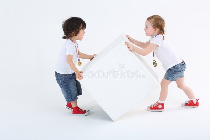 La petite fille et le garçon avec des médailles renversent le grand cube blanc photos libres de droits