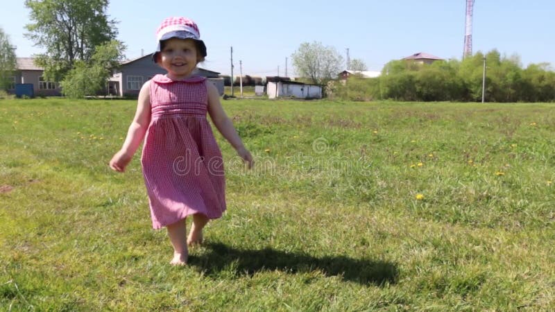 La petite fille heureuse va sur l'herbe verte au jour d'été ensoleillé