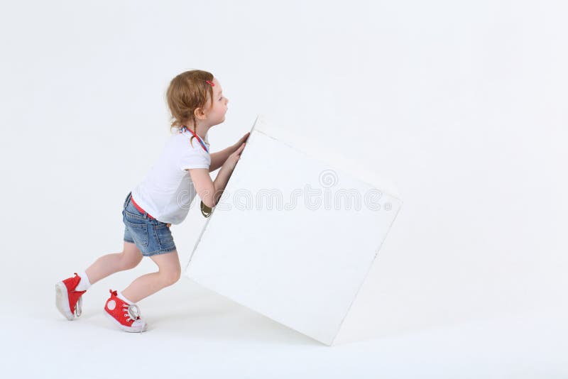 La petite fille mignonne dans des espadrilles pousse le grand cube blanc photographie stock libre de droits