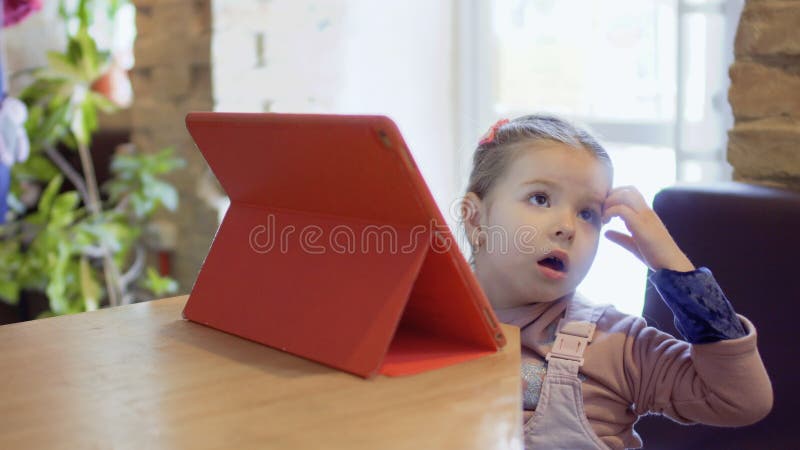 La petite fille mignonne utilise le comprimé numérique dans le café