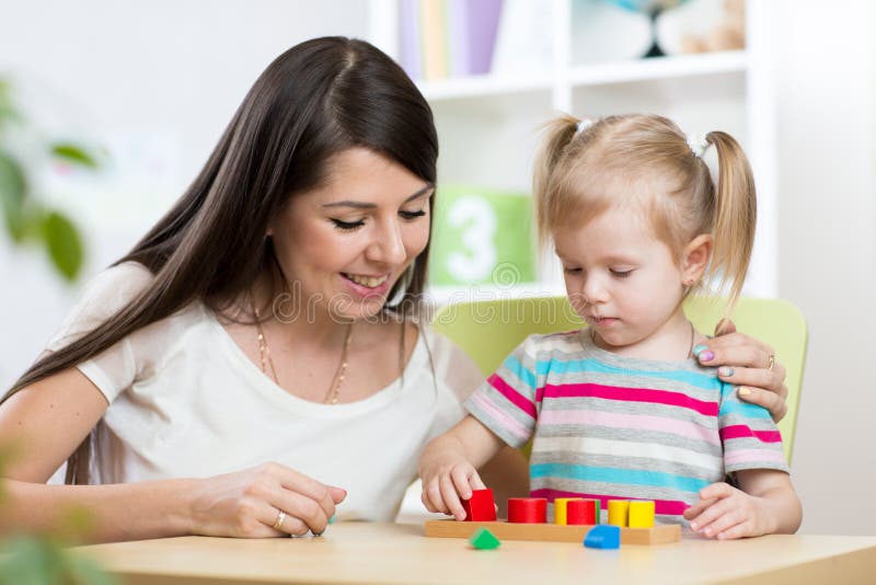 La petite fille résout le puzzle Mère observant à ses actions image libre de droits La petite fille résout le puzzle Mère observant à ses actions image libre de droits
