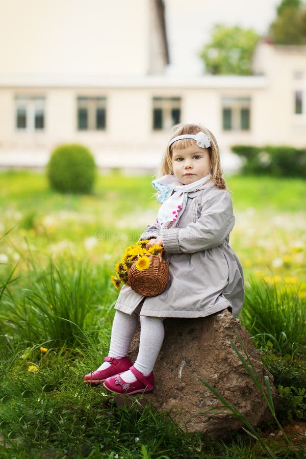 La petite fille s'assied sur une pierre avec un bouquet des pissenlits images libres de droits La petite fille s'assied sur une pierre avec un bouquet des pissenlits images libres de droits