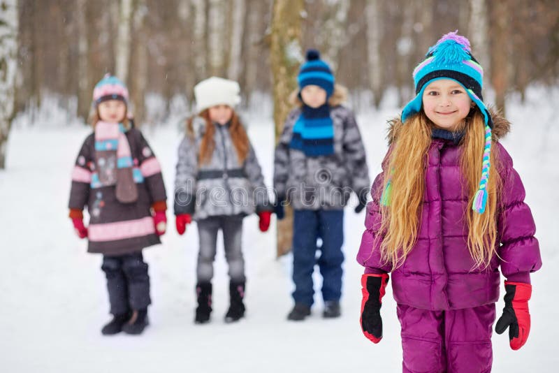 La petite fille se tient en parc d'hiver, amis se tiennent derrière images libres de droits La petite fille se tient en parc d'hiver, amis se tiennent derrière images libres de droits