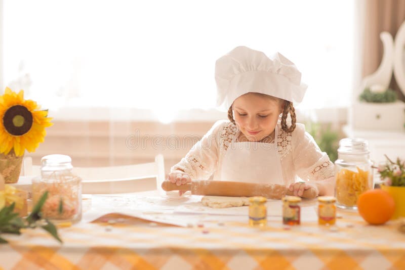 La petite fille sous forme de cuisinier déroule la pâte photographie stock libre de droits La petite fille sous forme de cuisinier déroule la pâte photographie stock libre de droits