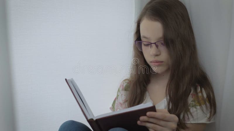 La petite fille sérieuse en verres fait diligemment son travail à la fenêtre