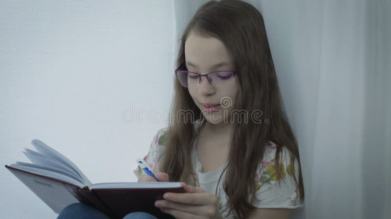 La petite fille émotive avec des verres écrit en son journal intime à la fenêtre