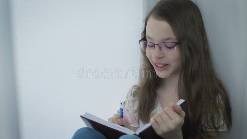 La petite fille émotive avec des verres écrit le journal intime et en riant