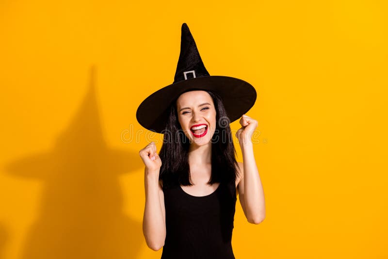 Photo of pretty lovely young magician lady raise fists scream yeah win masquerade, quiz excited achieve rare magic item wear black headwear dress isolated bright yellow color background. Photo of pretty lovely young magician lady raise fists scream yeah win masquerade, quiz excited achieve rare magic item wear black headwear dress isolated bright yellow color background