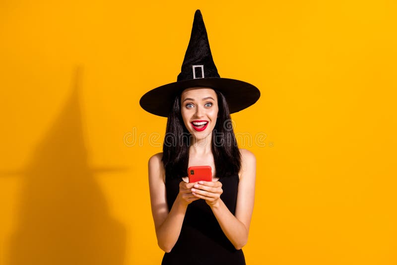 Photo of pretty lovely young magician lady hold telephone excited read holiday, post sharing friend liking wear black wizard headwear dress isolated bright yellow color background. Photo of pretty lovely young magician lady hold telephone excited read holiday, post sharing friend liking wear black wizard headwear dress isolated bright yellow color background