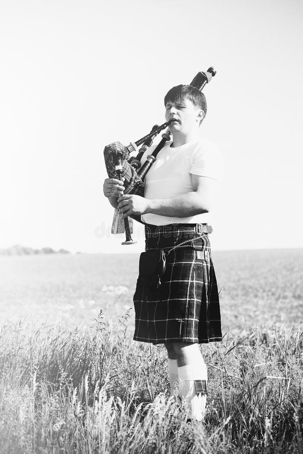 La photographie blanche noire de l'homme appréciant jouant siffle dans le kilt traditionnel écossais sur le champ d'été de l'espa photos stock La photographie blanche noire de l'homme appréciant jouant siffle dans le kilt traditionnel écossais sur le champ d'été de l'espa photos stock