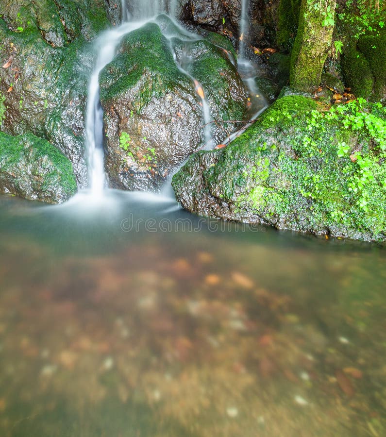 La piccola caduta serica dell'acqua che investe il muschio ha coperto le rocce fotografia stock libera da diritti La piccola caduta serica dell'acqua che investe il muschio ha coperto le rocce fotografia stock libera da diritti