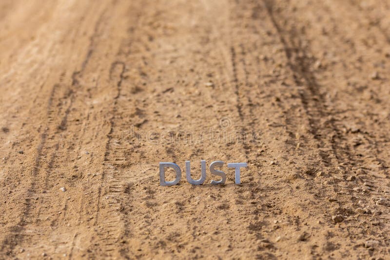 The word dust standing on dusty road surface in linear perspective with selective focus and background blur under direct sunlight. The word dust standing on dusty road surface in linear perspective with selective focus and background blur under direct sunlight