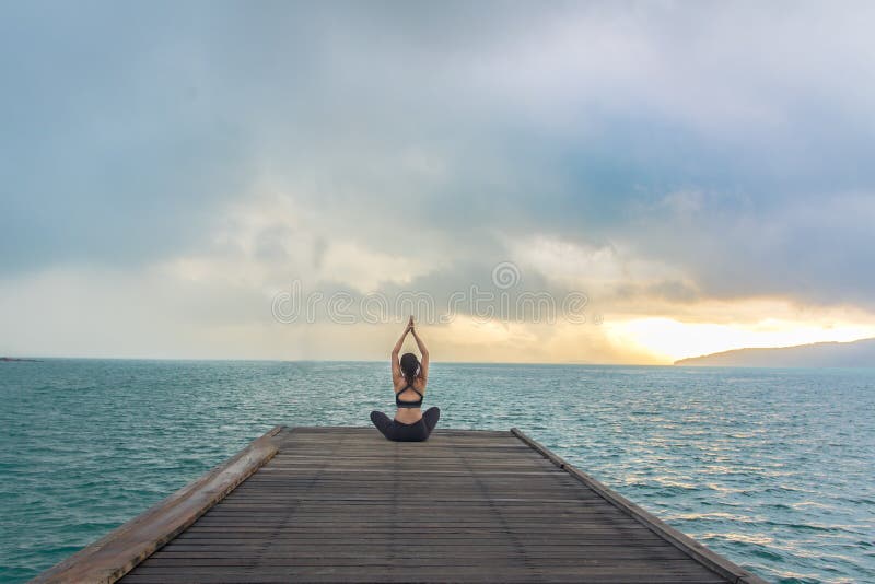 La pratica equilibrata stile di vita sano della donna meditano e l'yoga di energia su ponte di legno nella mattina la spiaggia fotografie stock libere da diritti La pratica equilibrata stile di vita sano della donna meditano e l'yoga di energia su ponte di legno nella mattina la spiaggia fotografie stock libere da diritti