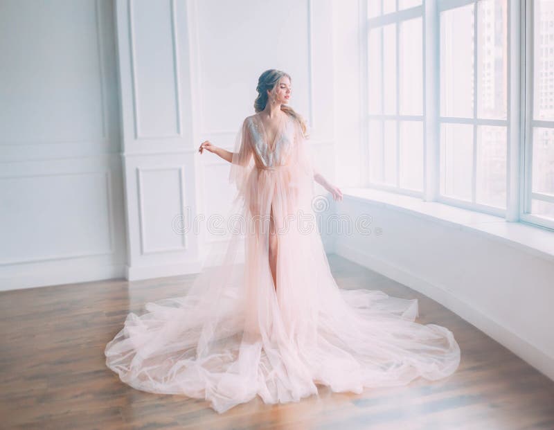 La princesse attirante mignonne avec les cheveux blonds dans la robe légère rose posant au soleil de la grande fenêtre, beauté de photos libres de droits La princesse attirante mignonne avec les cheveux blonds dans la robe légère rose posant au soleil de la grande fenêtre, beauté de photos libres de droits