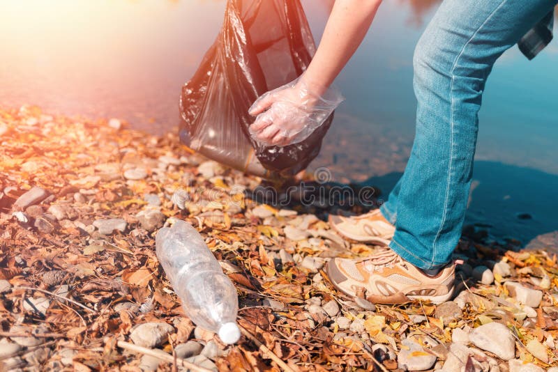 Environmental protection and earth day. A female volunteer removes a plastic bottle on the shore of a lake or river. Light. Environmental protection and earth day. A female volunteer removes a plastic bottle on the shore of a lake or river. Light.