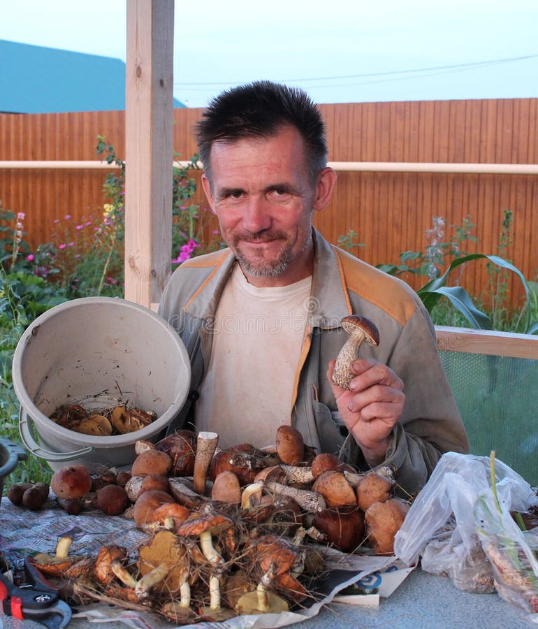 La raccoglitrice allegra del fungo dell'uomo ha riunito molti funghi commestibili a sorridere della tavola felice fotografia stock La raccoglitrice allegra del fungo dell'uomo ha riunito molti funghi commestibili a sorridere della tavola felice fotografia stock