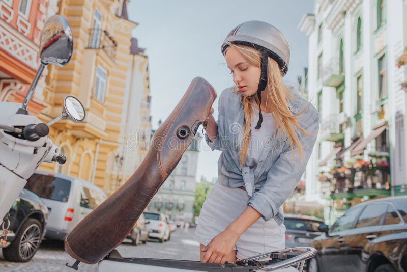 La ragazza astuta e bella sta guardando nell'ambito del sedile del motociclo Sta cercando qualcosa La ragazza stnding fuori sopra immagine stock libera da diritti La ragazza astuta e bella sta guardando nell'ambito del sedile del motociclo Sta cercando qualcosa La ragazza stnding fuori sopra immagine stock libera da diritti