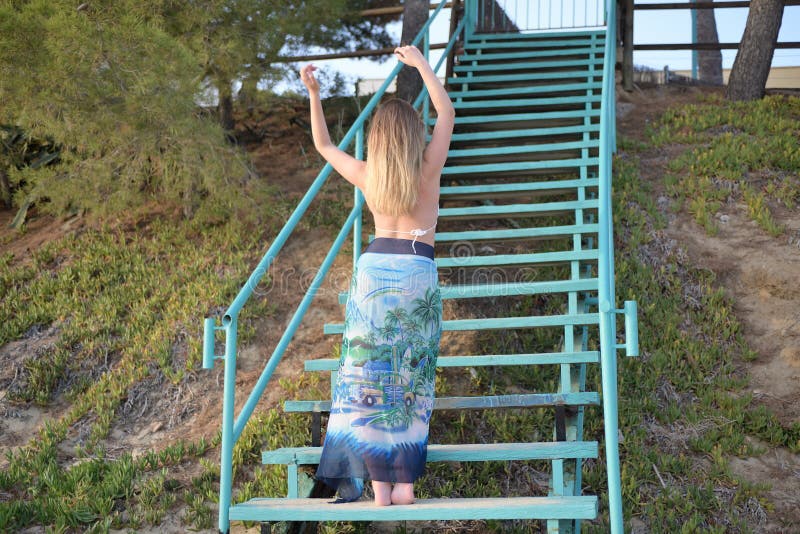 La ragazza bionda balla sensuale sulle scale di nuovo alla macchina fotografica con le armi alzate fotografie stock La ragazza bionda balla sensuale sulle scale di nuovo alla macchina fotografica con le armi alzate fotografie stock