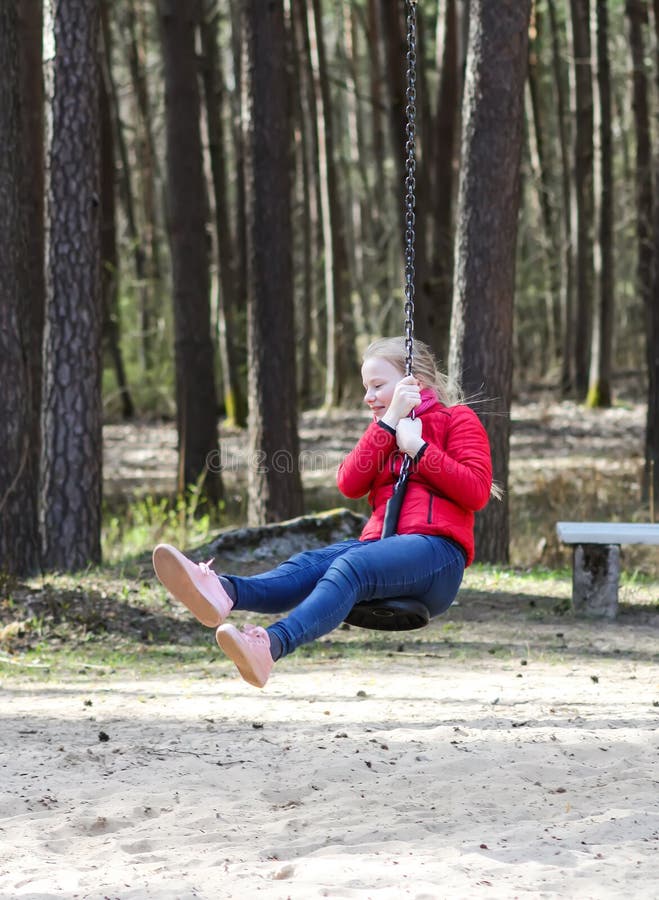 La ragazza bionda felice dell'adolescente si è vestita in rivestimento rosso e blue jeans che saltano e che guidano giù con l'amm immagini stock La ragazza bionda felice dell'adolescente si è vestita in rivestimento rosso e blue jeans che saltano e che guidano giù con l'amm immagini stock