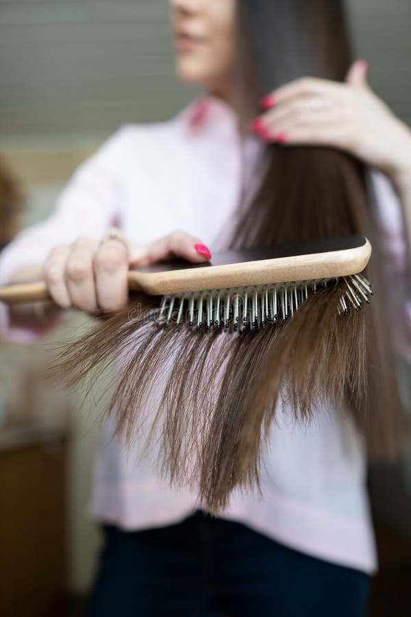 La ragazza castana in una camicia rosa sta pettinando il suo bello pettine lungo dei capelli fotografia stock libera da diritti La ragazza castana in una camicia rosa sta pettinando il suo bello pettine lungo dei capelli fotografia stock libera da diritti