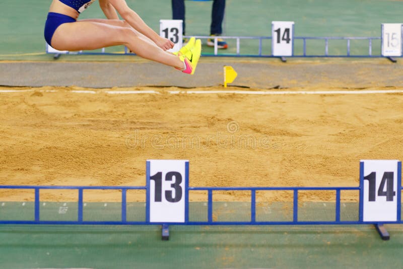 La ragazza che salta nella sabbionaia sulla concorrenza di salto in lungo immagini stock La ragazza che salta nella sabbionaia sulla concorrenza di salto in lungo immagini stock