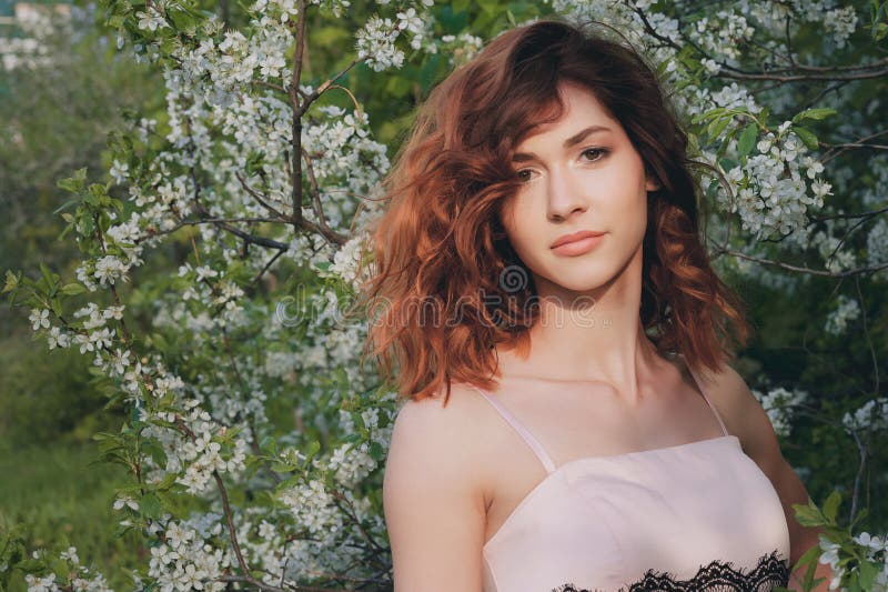 La ragazza con capelli rosso scuro splendidi su un fondo di verde fiorisce la natura Di melo in fioritura Giardino della sorgente immagine stock libera da diritti La ragazza con capelli rosso scuro splendidi su un fondo di verde fiorisce la natura Di melo in fioritura Giardino della sorgente immagine stock libera da diritti