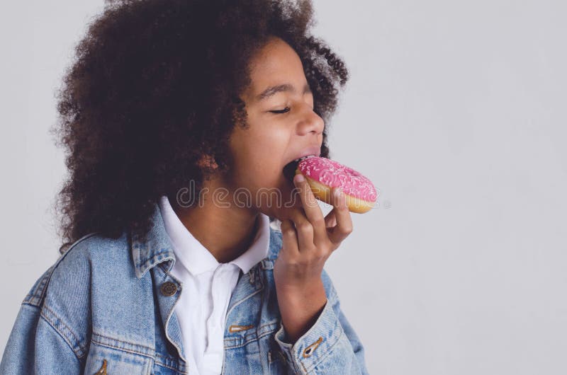 La ragazza dalla carnagione scura morde una ciambella con una glassa rosa fotografia stock La ragazza dalla carnagione scura morde una ciambella con una glassa rosa fotografia stock