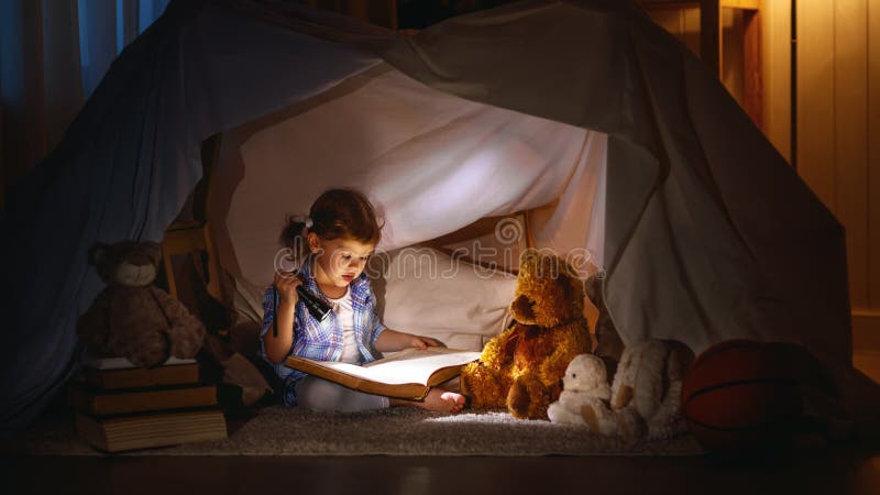 La ragazza del bambino con un libro e una torcia elettrica e l'orsacchiotto prima vanno