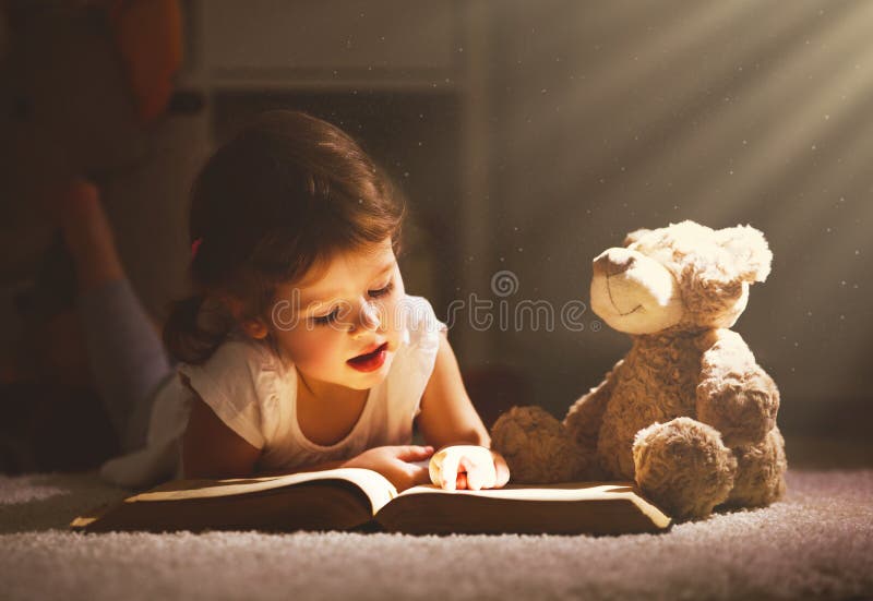 La ragazza del piccolo bambino sta leggendo un libro nella sera nello scuro con la a a fotografie stock libere da diritti
