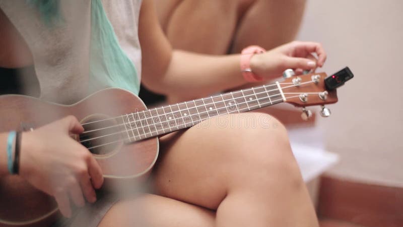 La ragazza di seduta in breve sintonizza la chitarra marrone delle ukulele sulla via Giorno pieno di sole di estate Musica string