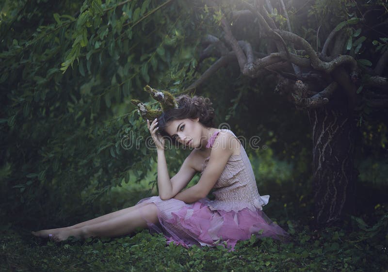La ragazza ha incantato principessa con i corni che si siedono sotto un albero Fawn mistico della creatura della ragazza in vesti