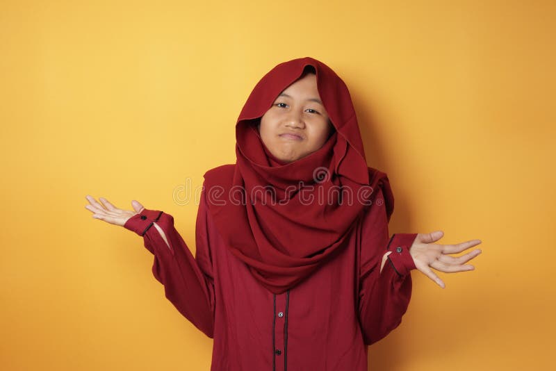 Portrait of teenage Asian muslim girl wearing hijab shows refusal or denial gesture, shoulder shrug, I don& x27;t know expression, against yellow background. Portrait of teenage Asian muslim girl wearing hijab shows refusal or denial gesture, shoulder shrug, I don& x27;t know expression, against yellow background