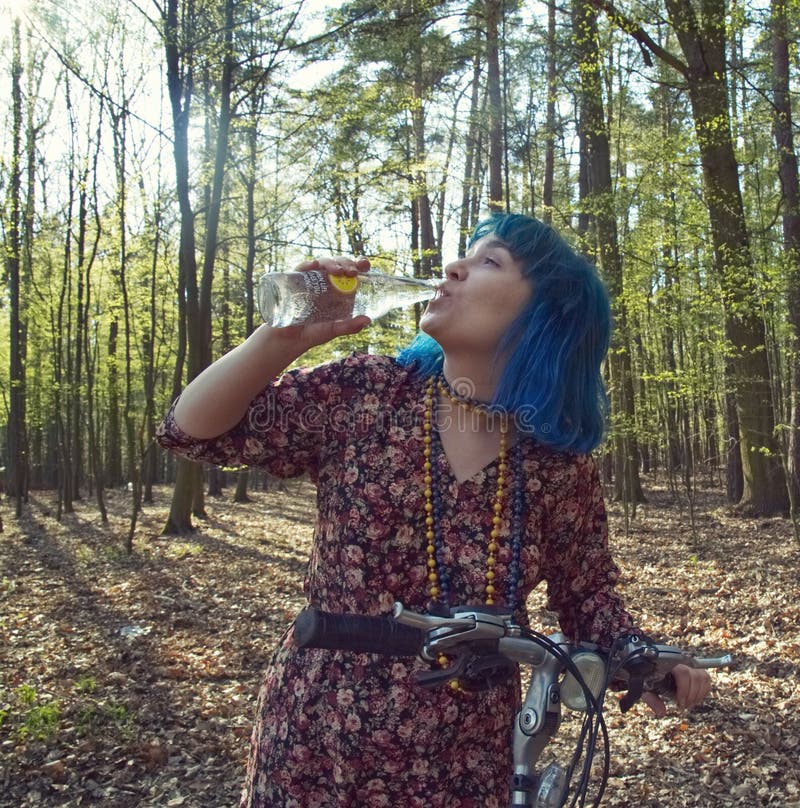La ragazza nella foresta, su una bici, beve l'acqua da una bottiglia fotografie stock libere da diritti La ragazza nella foresta, su una bici, beve l'acqua da una bottiglia fotografie stock libere da diritti
