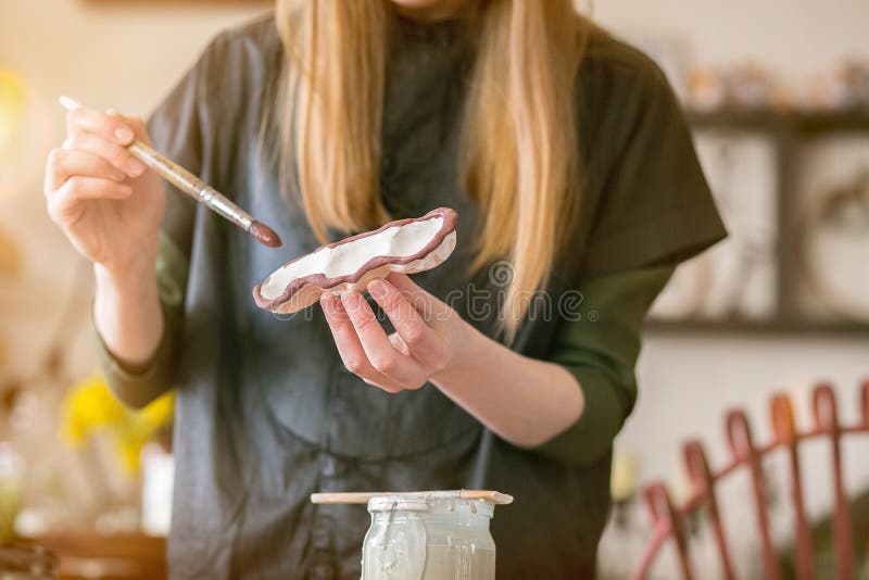 La ragazza pennelli con terraglie ceramiche nell'officina creativa immagine stock libera da diritti La ragazza pennelli con terraglie ceramiche nell'officina creativa immagine stock libera da diritti