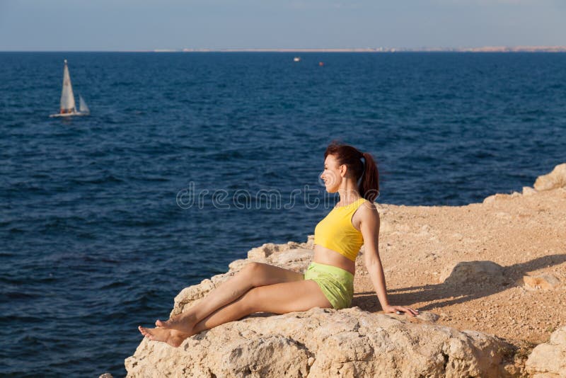 La ragazza si siede su una scogliera e sull'esame del mare fotografia stock libera da diritti La ragazza si siede su una scogliera e sull'esame del mare fotografia stock libera da diritti