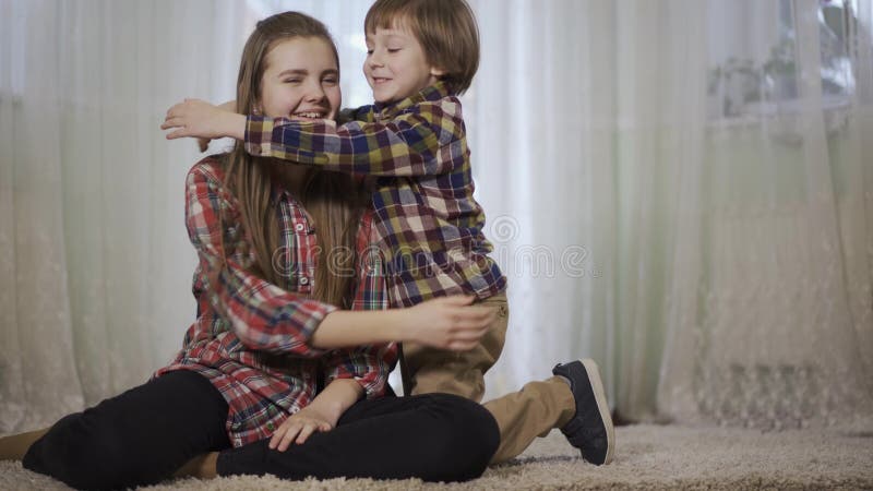 La ragazza si siede sulla coperta lanuginosa nel salone ed suo fratello viene a stringerlo a sé Amore e felicità della famiglia