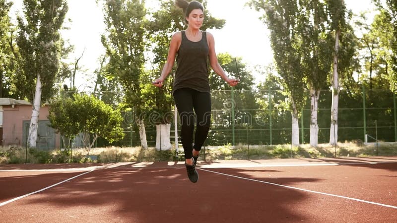 La ragazza sportiva di brinette che si esercita con una corda di salto, saltante su, fa scorrere la corda parecchie volte All'ape stock footage