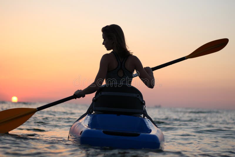 La ragazza sul kajak accoglie l'alba del sole immagini stock libere da diritti La ragazza sul kajak accoglie l'alba del sole immagini stock libere da diritti