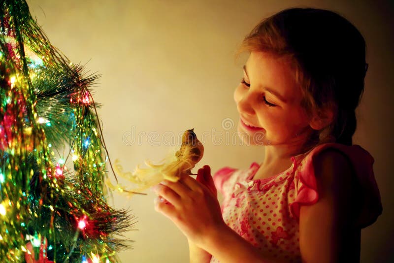 La ragazza sveglia sorridente tiene l'uccello del giocattolo accanto all'albero di Natale fotografia stock libera da diritti La ragazza sveglia sorridente tiene l'uccello del giocattolo accanto all'albero di Natale fotografia stock libera da diritti