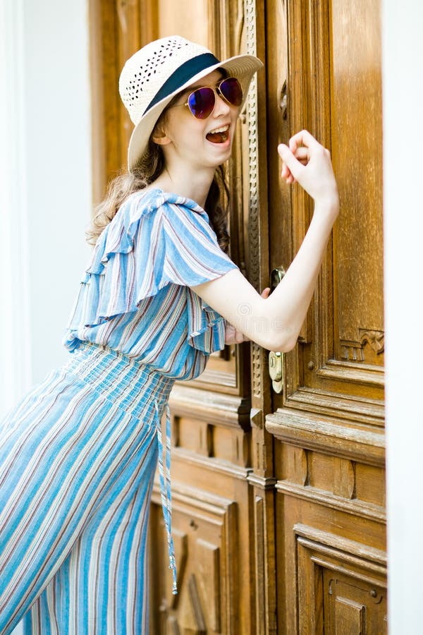La ragazza Teenaged in vestito dalla tuta sta battendo sulla porta d'annata fotografia stock La ragazza Teenaged in vestito dalla tuta sta battendo sulla porta d'annata fotografia stock