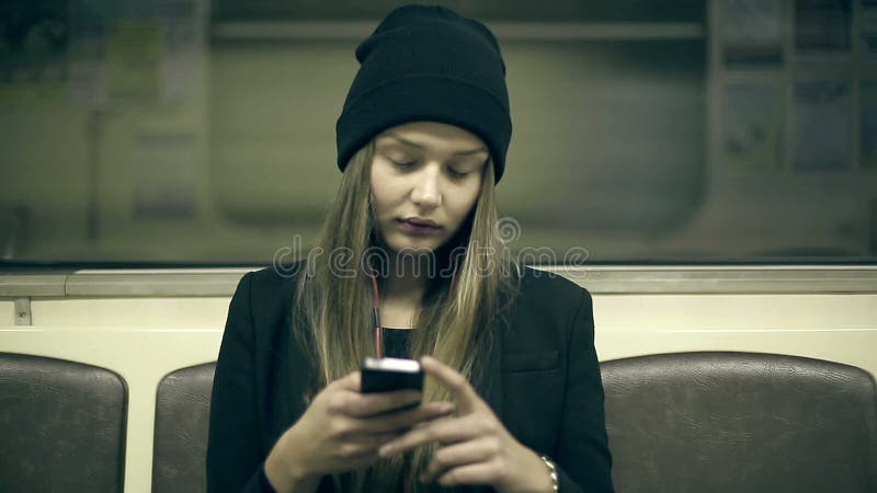 La ragazza teenager guida la metropolitana alla notte ed allo smartphone utilizzato