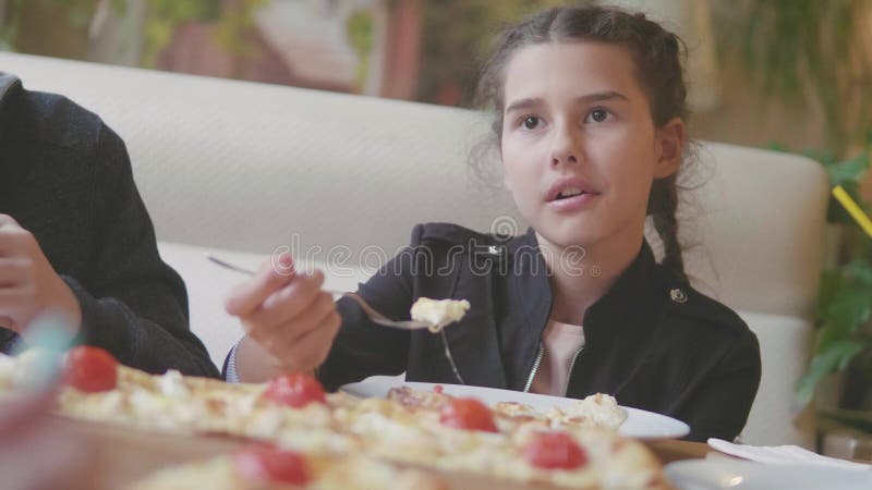 La ragazza teenager mangia la pizza in video di movimento lento del caffè i bambini mangiano la pizza una pizza deliziosa società